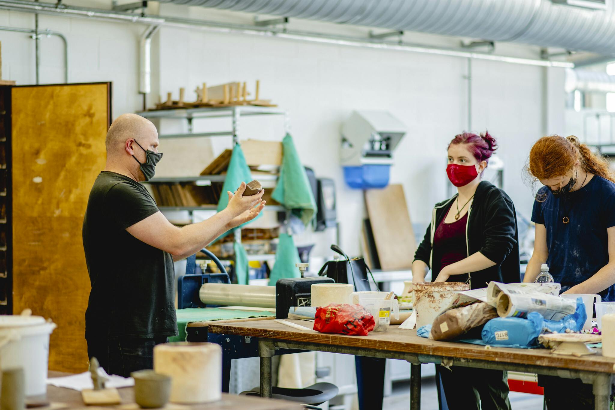 Technician Dan Chapple shows two students examples of clay in the Plymouth College of Art ceramics studio. The table in the centre is filled with the students ceramic creations and tools for ceramics