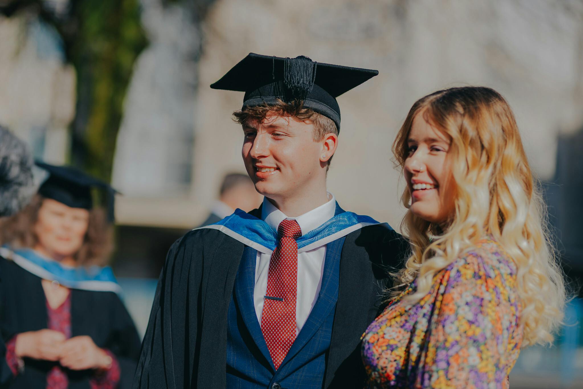 A male student wearing a graduation gown and cap smiles standing next to a smiling woman with blonde hair at the Arts University Plymouth Graduation Ceremony 2023