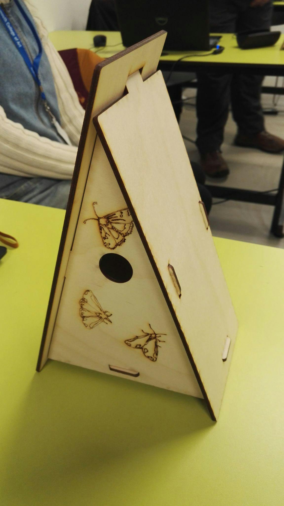 Image shows a lazer cut bird house in a triangle A frame type design made out of wood
