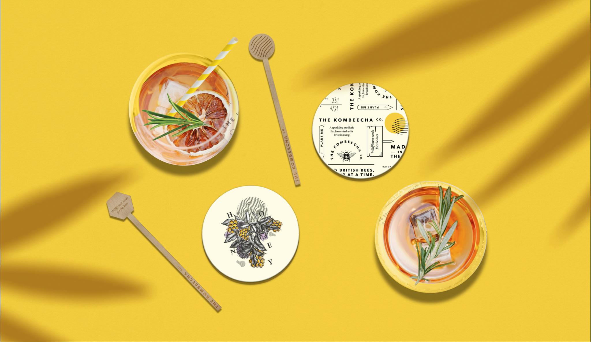 Image shows an overhead view of cocktails featuring stirrers and coasters with the Kombeecha Co. branding which features an illustrated bee and typography