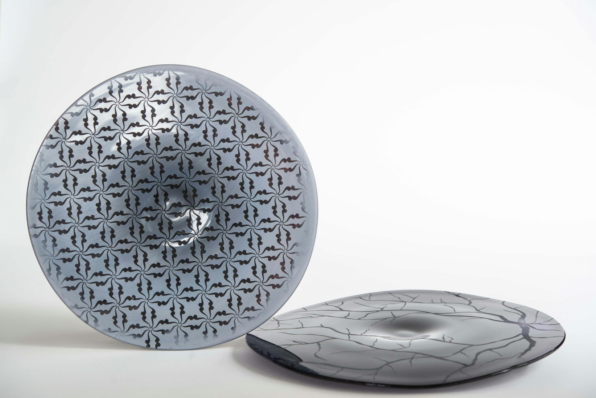 Image shows two glass discs in shades of bluey grey, one flat on the surface, another on its edge, with etchings and patterns