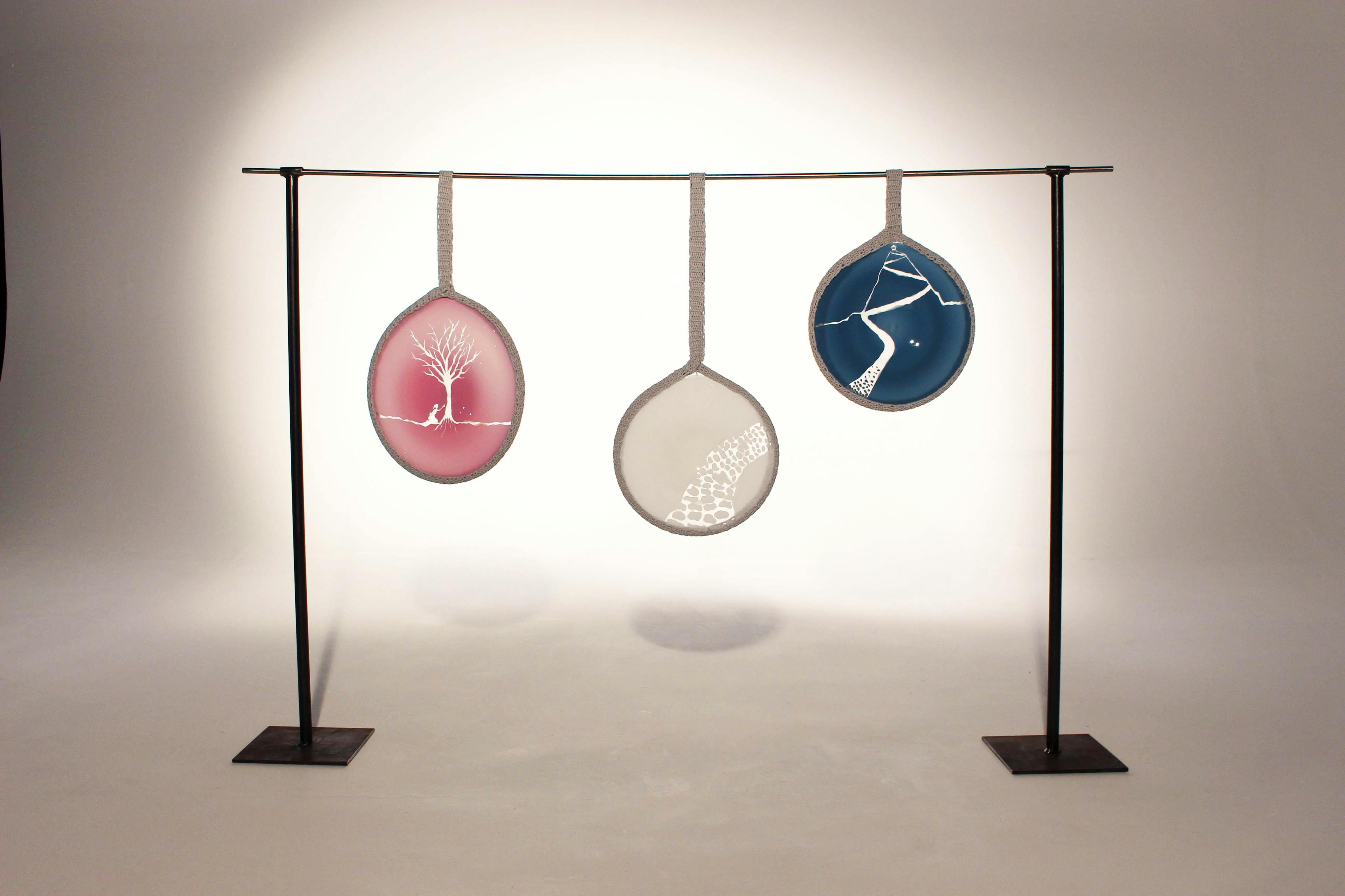 Image shows three glass discs in different colour and with natural etchings and detail hanging from a black metal frame